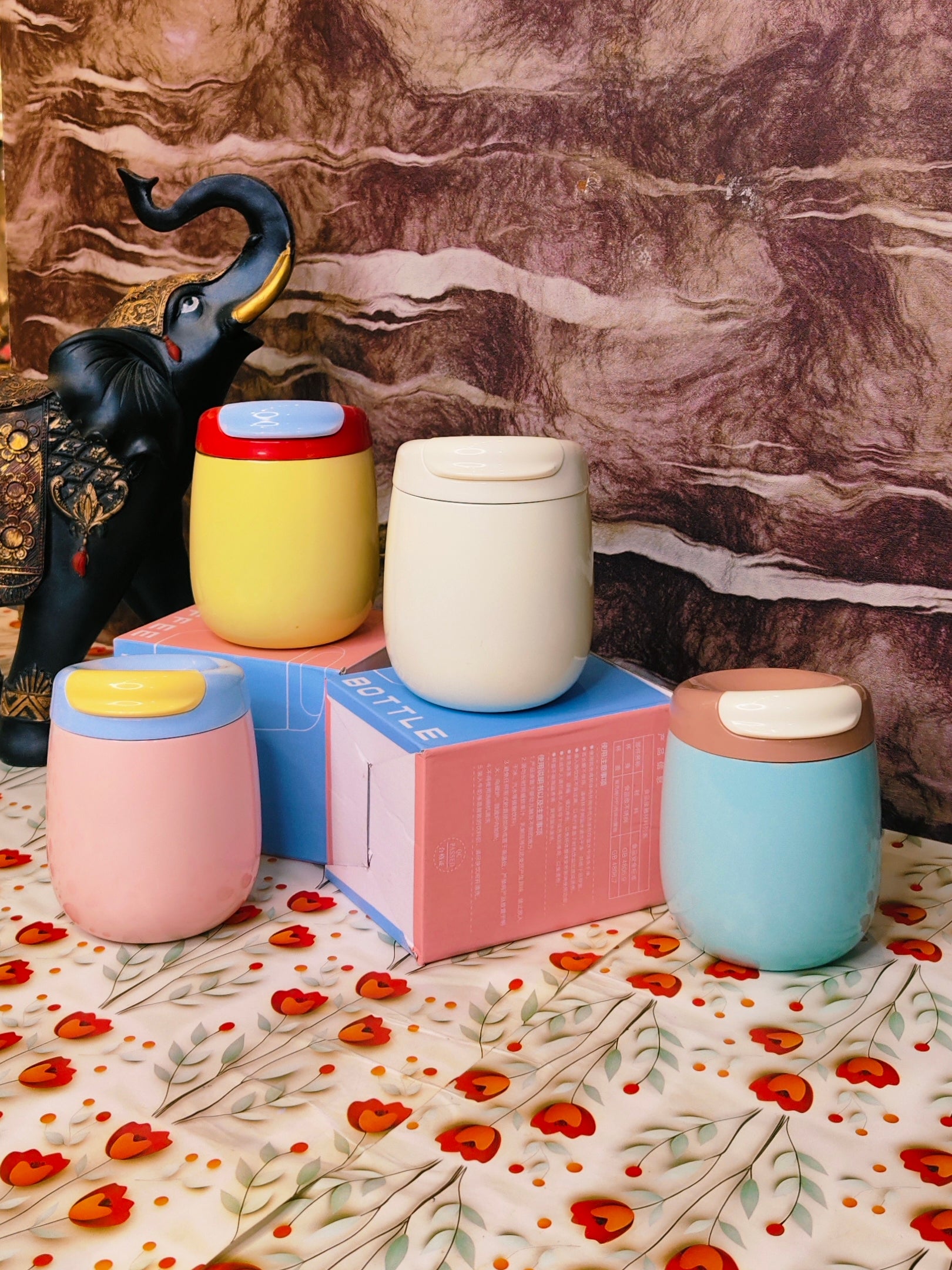 Colorful steel tumblers on a floral-patterned surface with a marble background