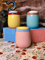 Three colorful steel tumblers with lids on a floral-patterned surface.