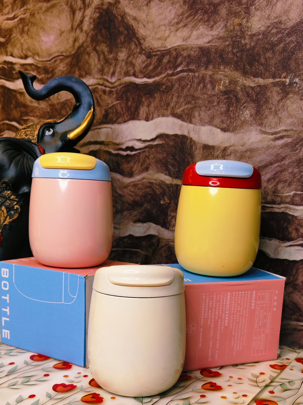 Three colorful steel tumblers on a floral-patterned surface with a textured brown background.