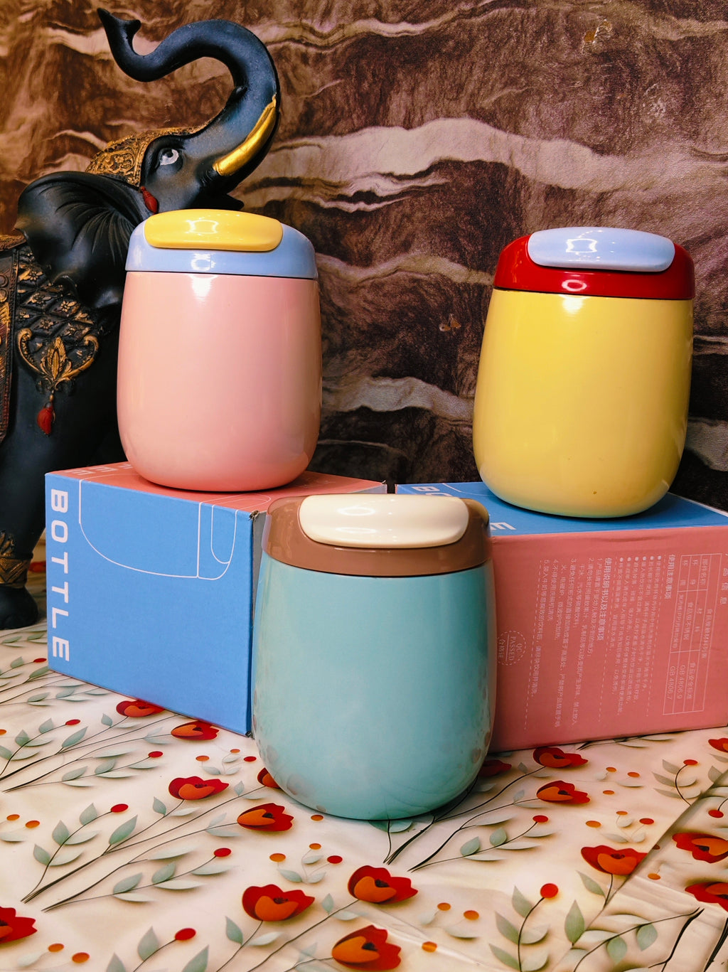 Three colorful steel tumblers with lids on a floral-patterned surface.