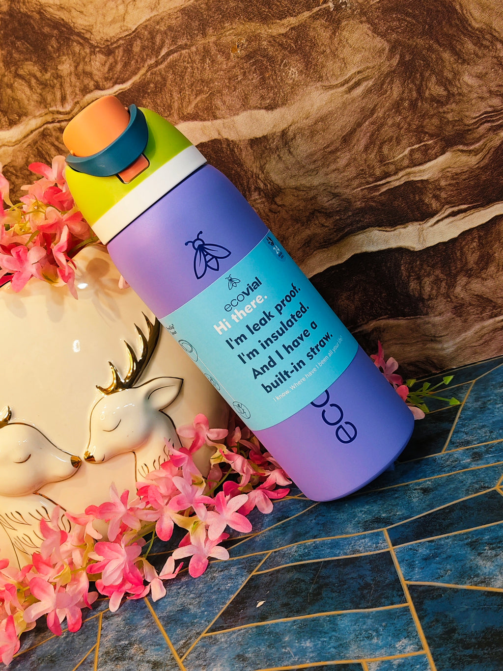 Purple insulated water bottle with text on a decorative surface with flowers and a deer figurine.