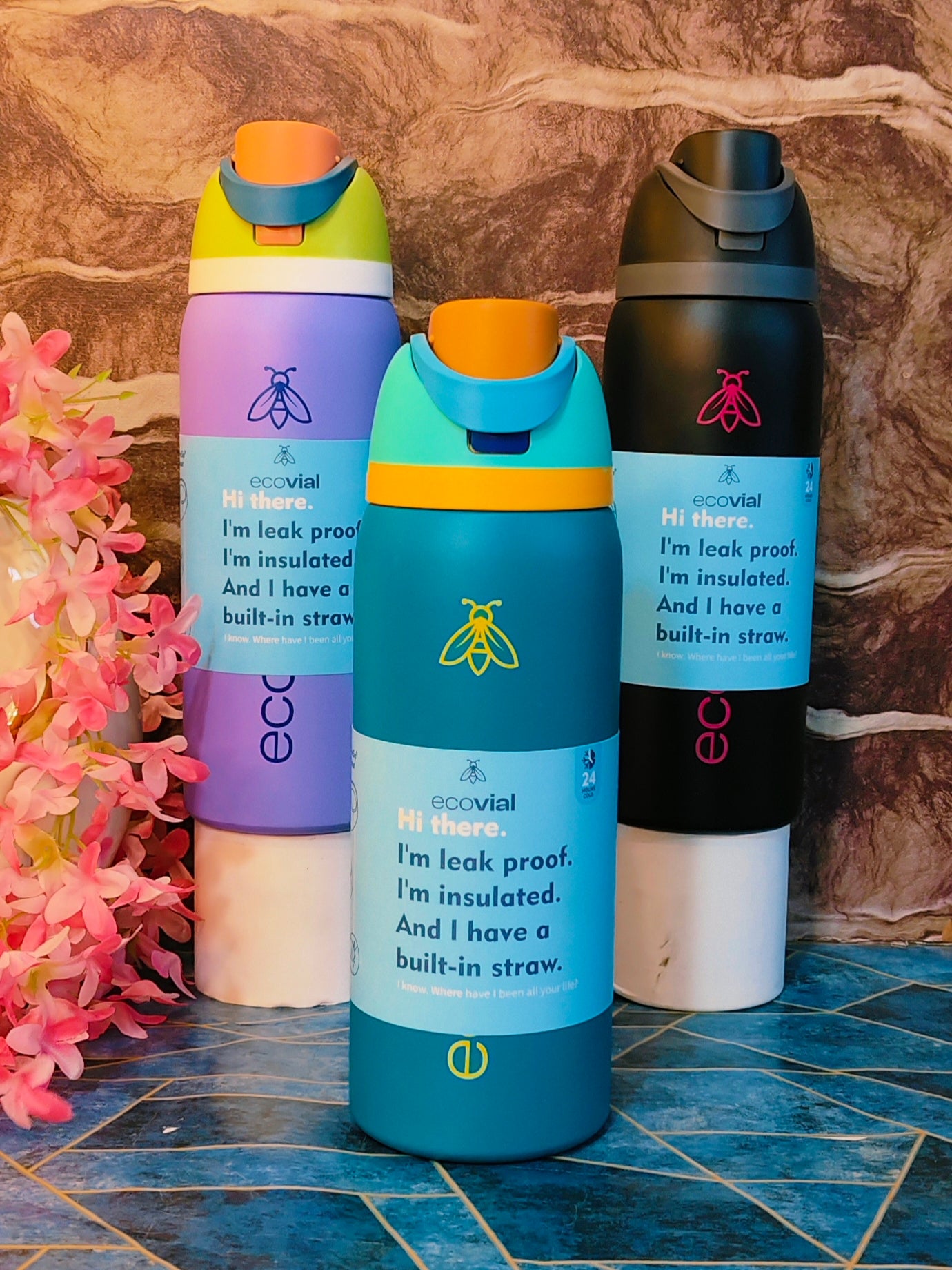 Three colorful water bottles with built-in straws on a textured surface.