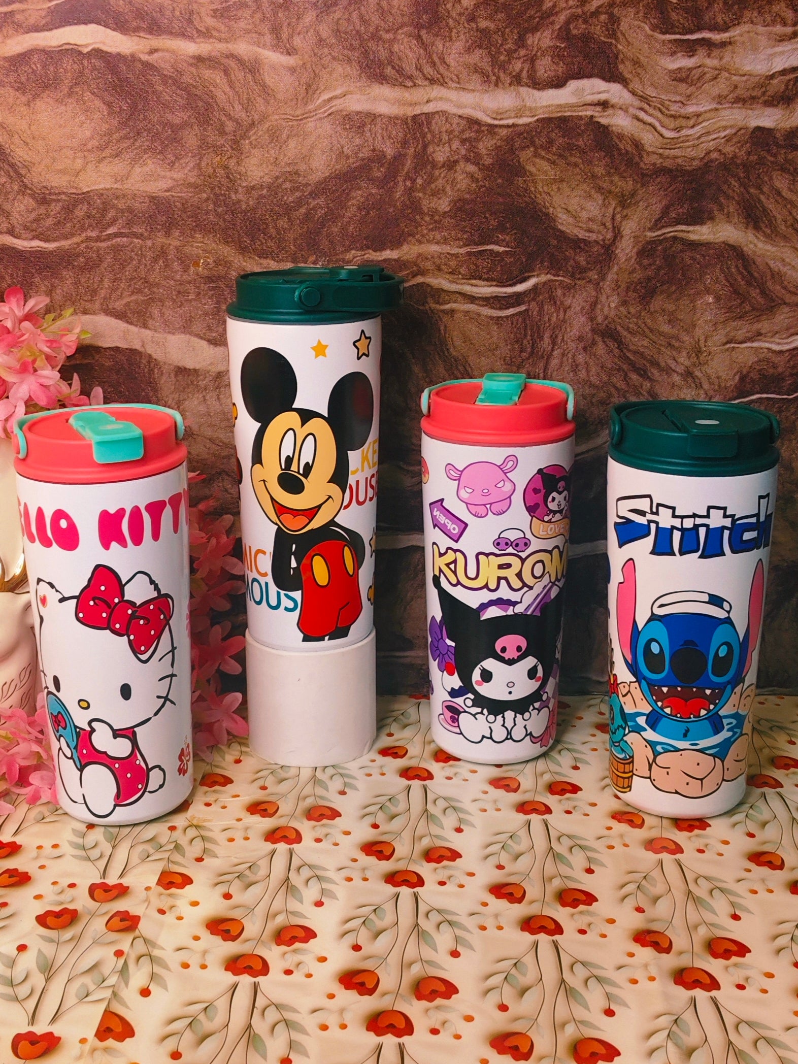 Four cartoon-themed tumblers on a floral-patterned surface with a brown textured background.
