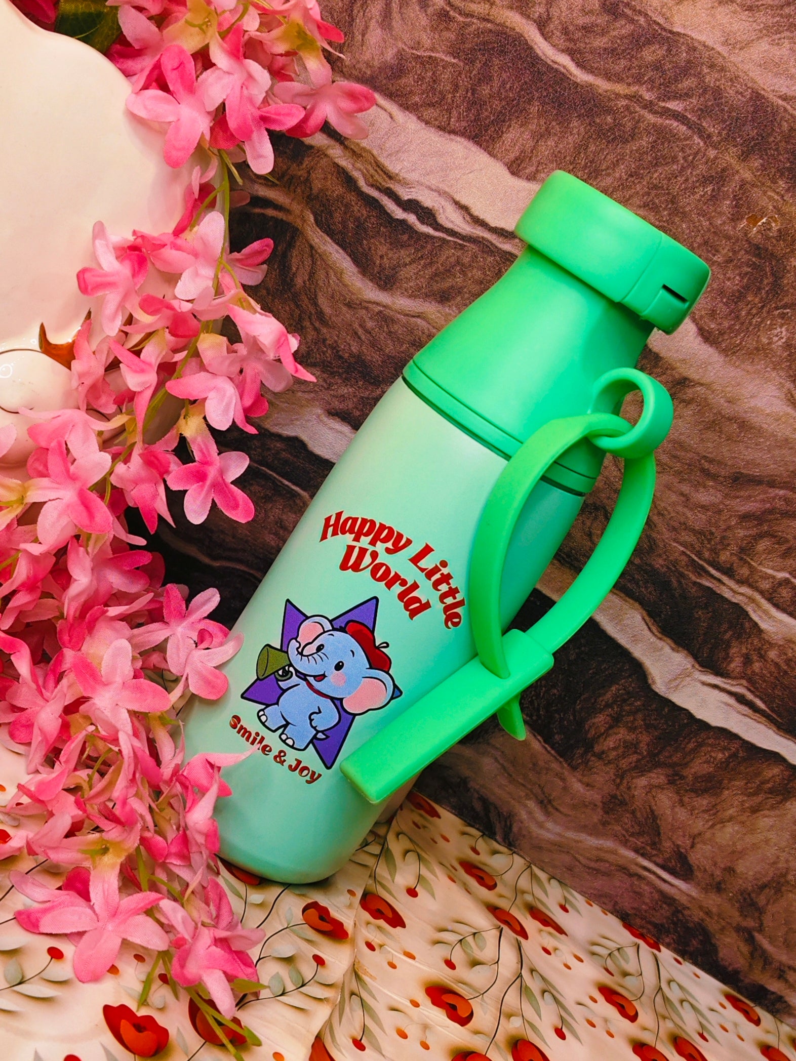 Green water bottle with cartoon character and text, surrounded by pink flowers on a marble surface
