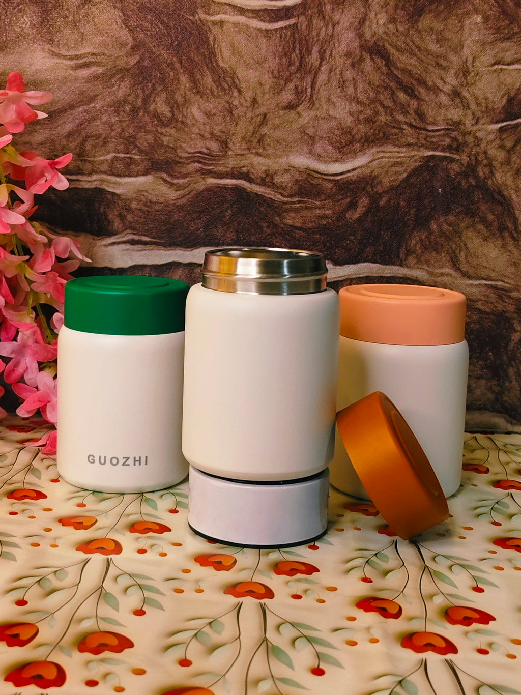 Three insulated containers with different colored lids on a floral-patterned surface.