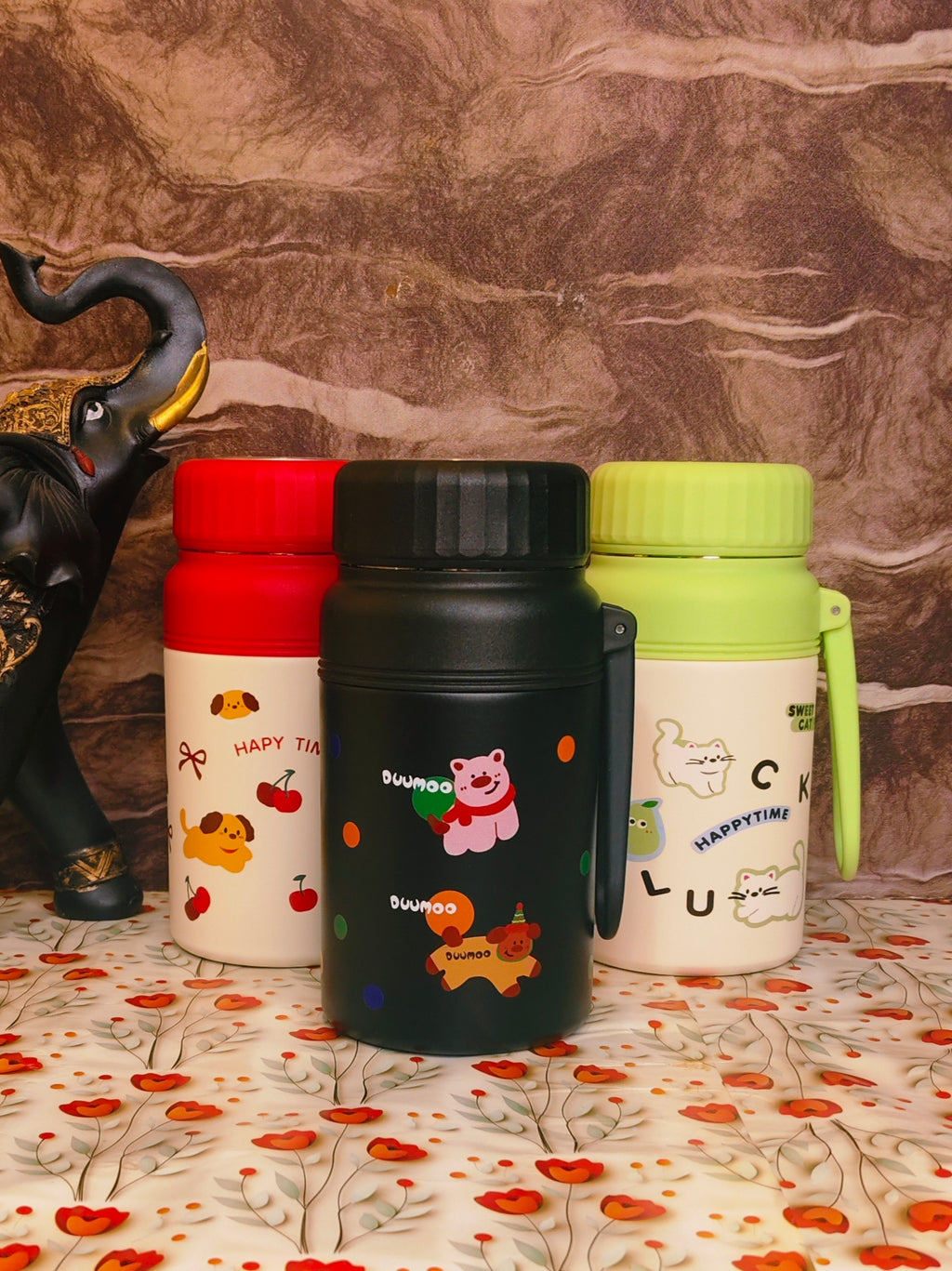 Three colorful thermos bottles with cartoon designs on a patterned surface.