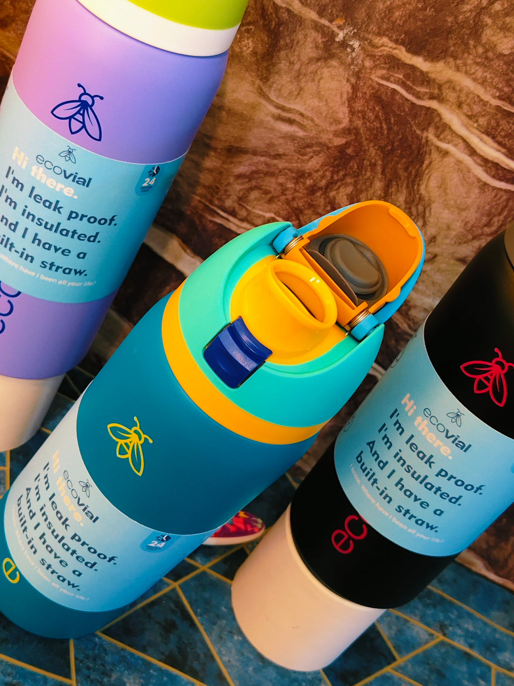 Three colorful water bottles with labels ecovial  on a textured surface
