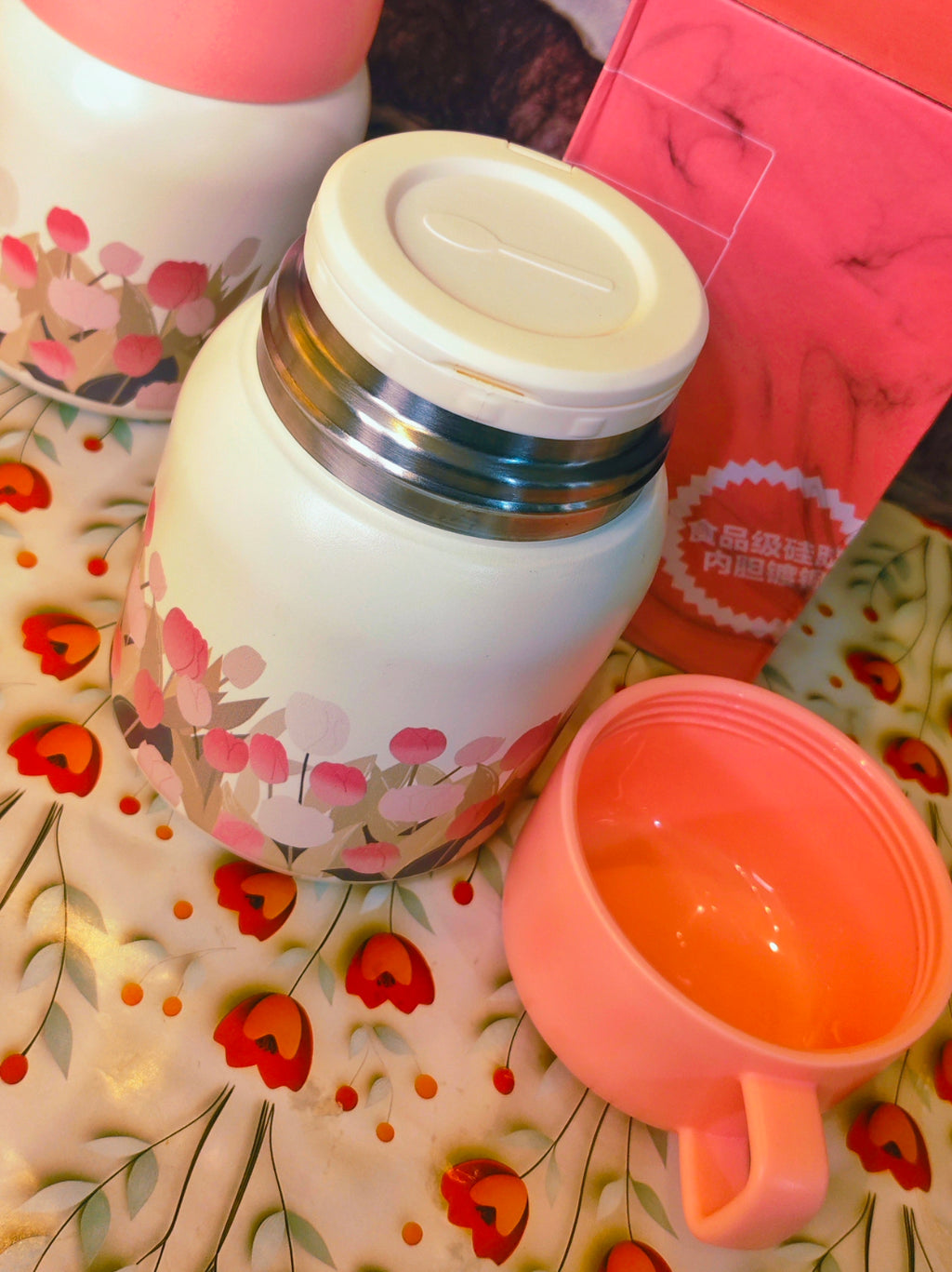 Floral-patterned thermos and pink cup on a floral tablecloth