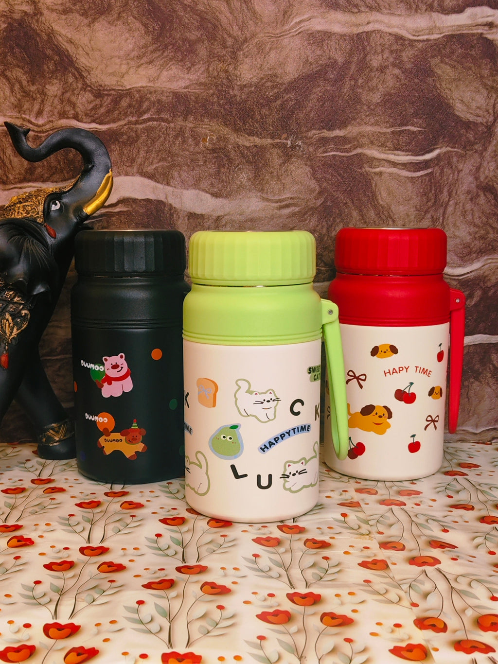 Three colorful thermos bottles with cartoon designs on a floral surface.