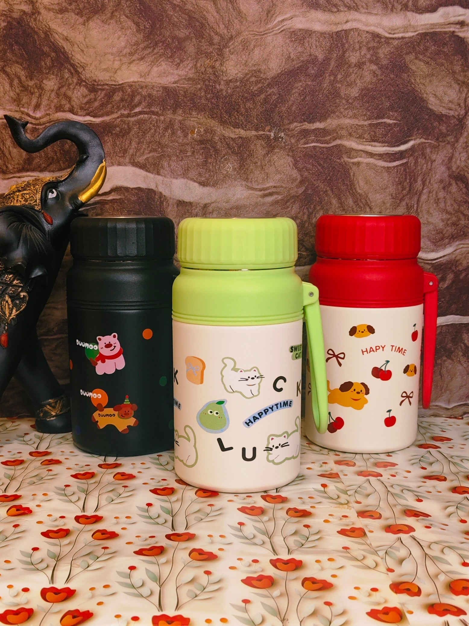 Three colorful thermos bottles with cartoon designs on a floral surface.